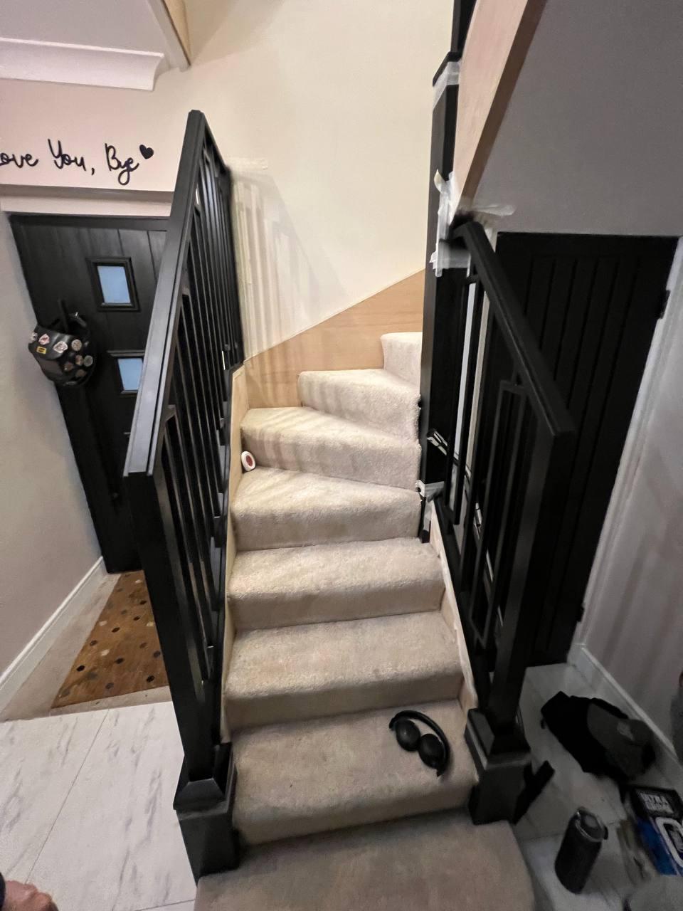 Front view of a carpeted staircase framed by bespoke black steel railings with clean vertical lines and geometric details.