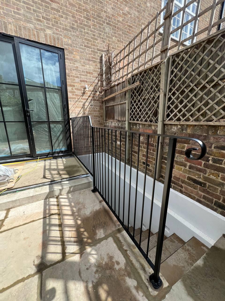 Black exterior stair balustrade showing the curled handrail termination