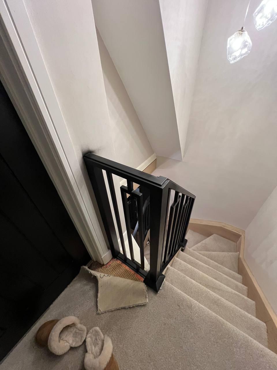 Black steel balustrade wrapping around the upper landing and staircase, featuring slim vertical bars and rectangular geometric accents.