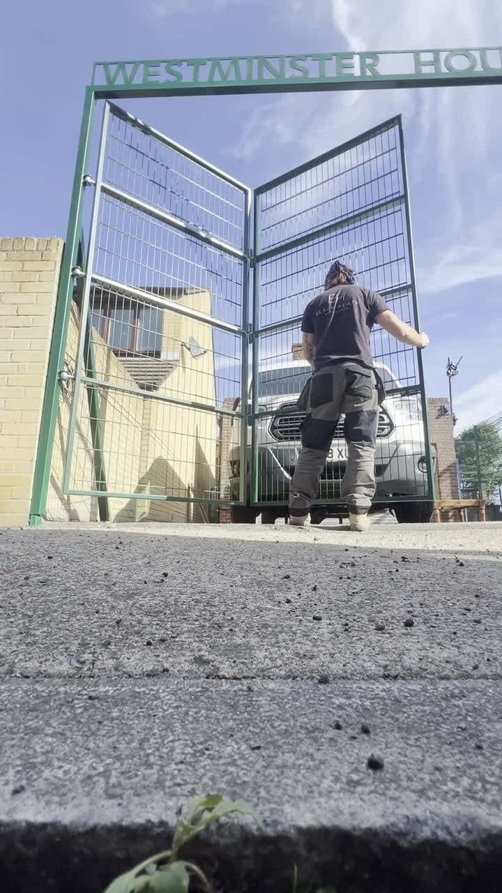 Black Heath Metalworks team member folding the installed green driveway gate at the youth club entrance