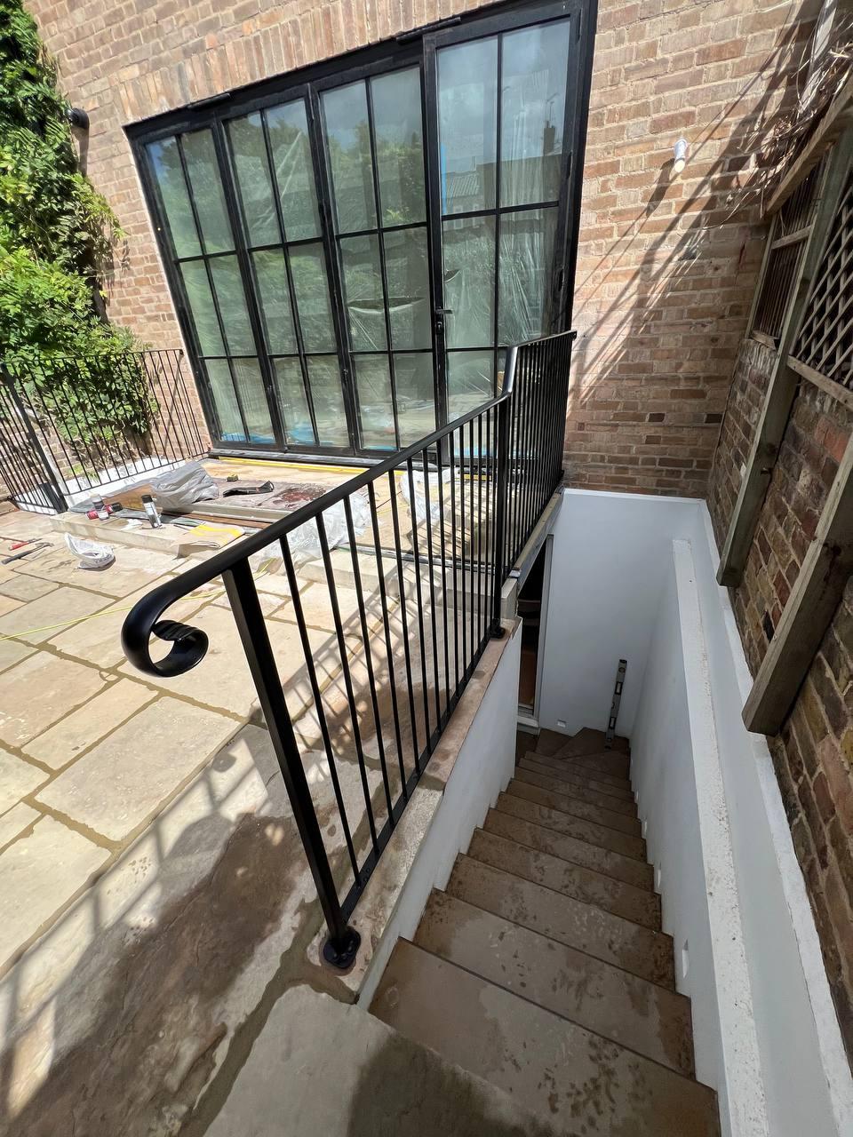 Black vertical-bar balustrade with a formed scroll end guarding an exterior basement stair