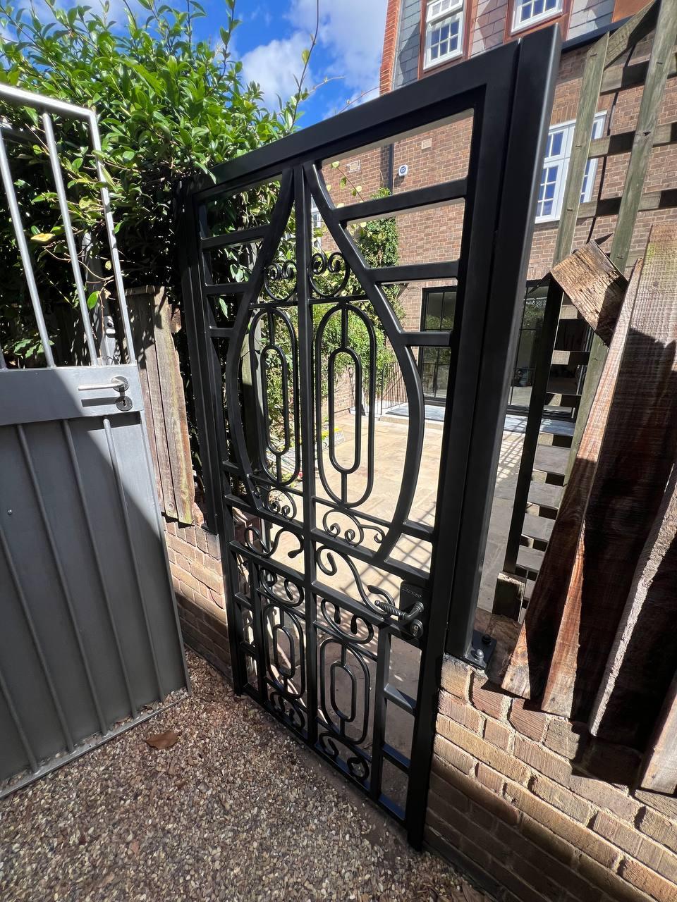 Rear view of the black garden gate showing its symmetrical oval motifs, scrollwork, rectangular frame and fitted handle.