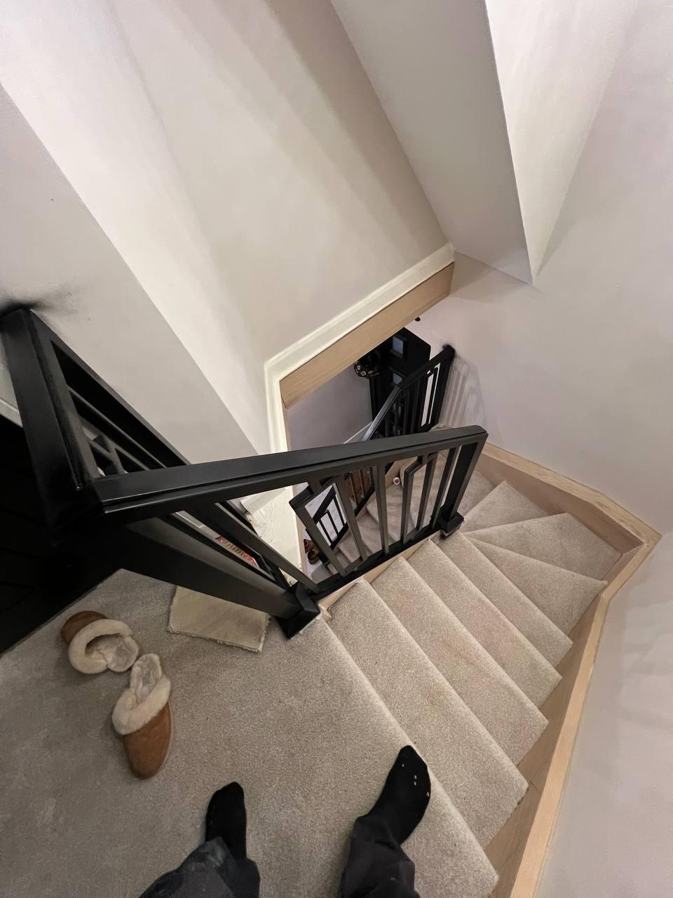 View from the upper landing of a bespoke black steel staircase balustrade with geometric detailing, set against pale timber trim and neutral carpet.
