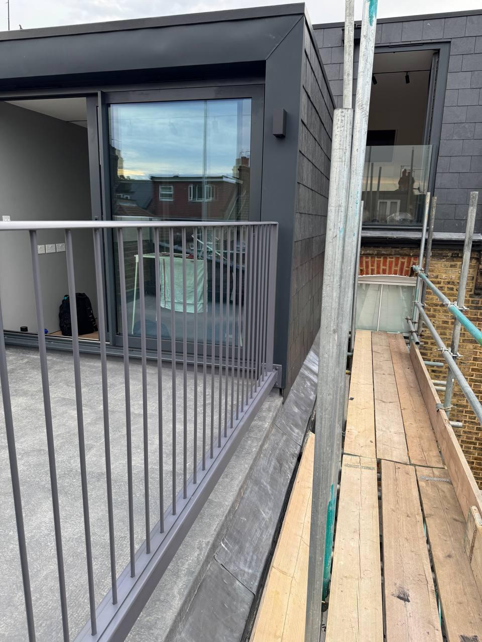 Side view of dark-grey metal terrace railings installed beside a contemporary rooftop extension.